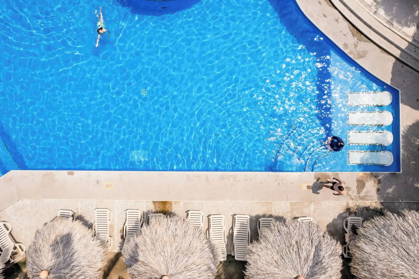 Overhead view of a bright blue pool with loungers and palapa shade at Hotel Castillo Huatulco & Beach Club.