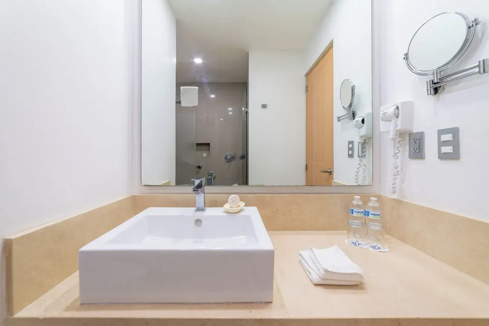 Standard Room bathroom vanity with square sink, mirror, towels, and shower view at Hotel Castillo Huatulco & Beach Club.
