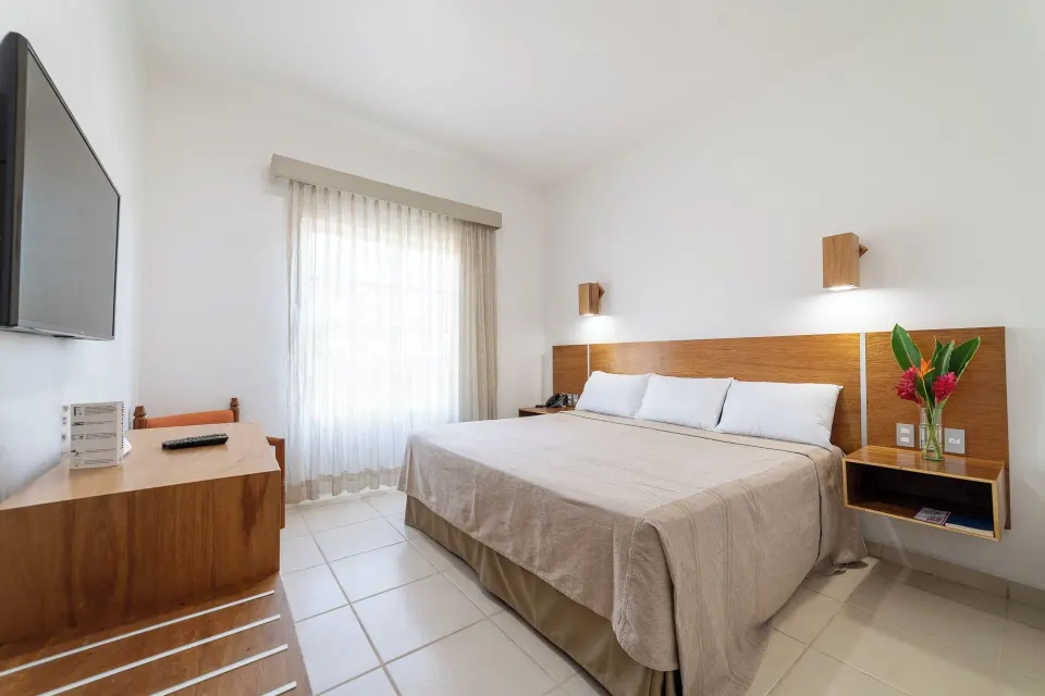 Standard Room with king bed, TV, dresser, bedside flowers, and window at Hotel Castillo Huatulco & Beach Club.