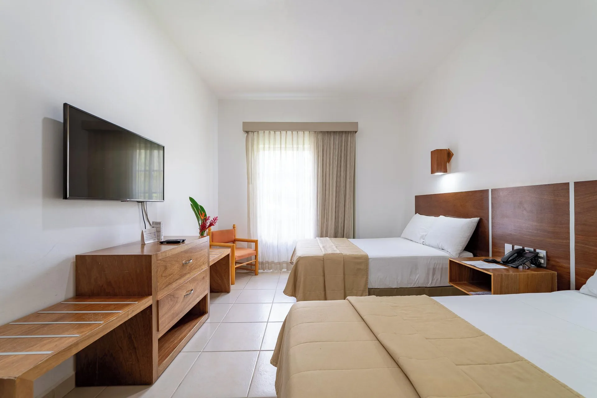 Standard Room with two beds, wall-mounted TV, dresser, chair, and window at Hotel Castillo Huatulco & Beach Club.