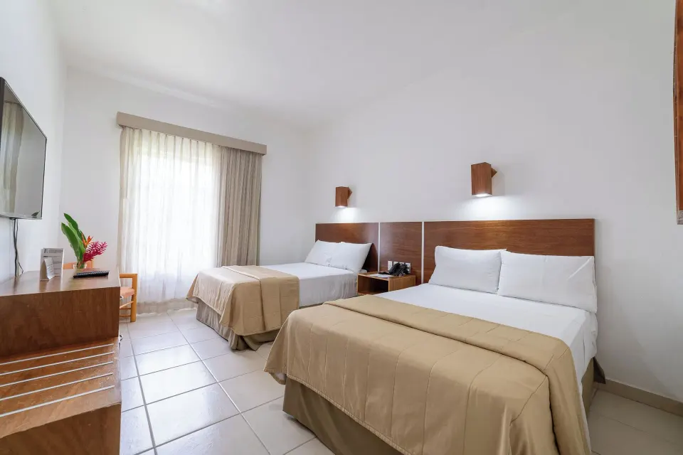 Standard Room with two beds, wall TV, dresser, and curtained window at Hotel Castillo Huatulco & Beach Club.