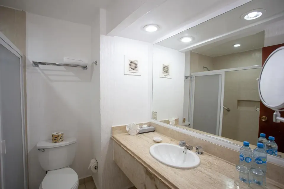 Standard room bathroom with sink, mirror, toilet, and shower at Hotel Castillo Huatulco & Beach Club.