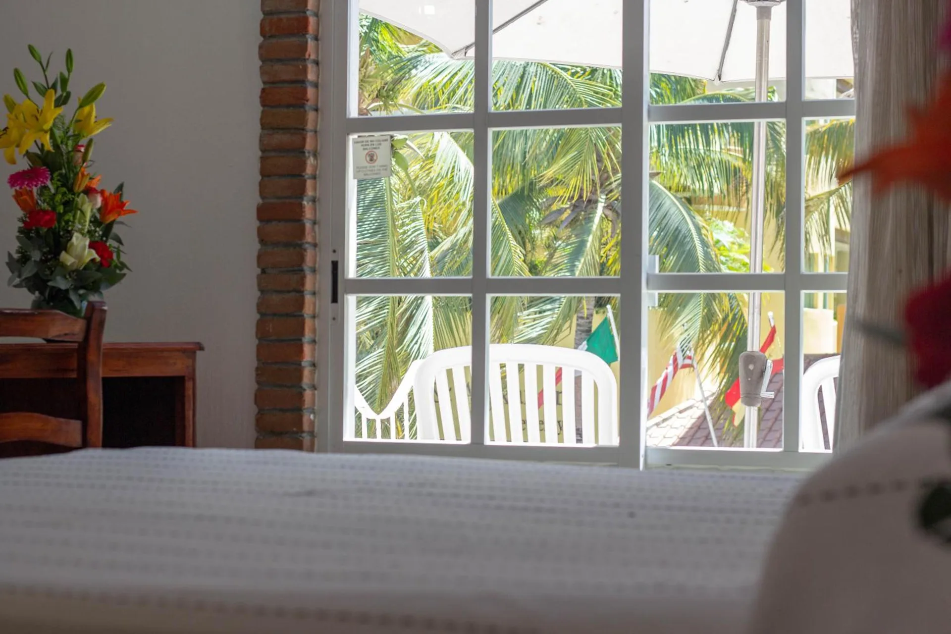 Standard room bed facing glass doors, balcony chairs, and palms at Hotel Castillo Huatulco & Beach Club.