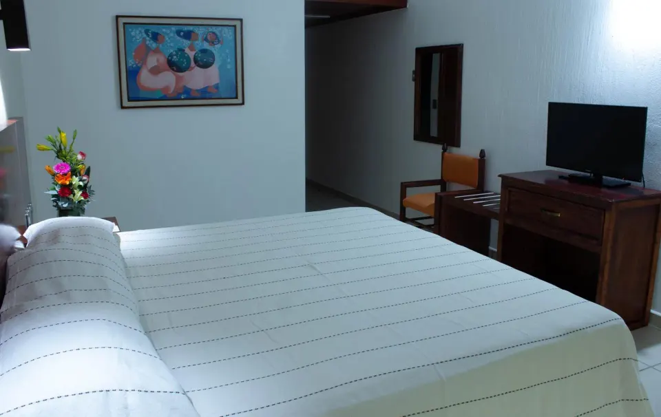 Standard room bed with TV dresser and chair at Hotel Castillo Huatulco & Beach Club.