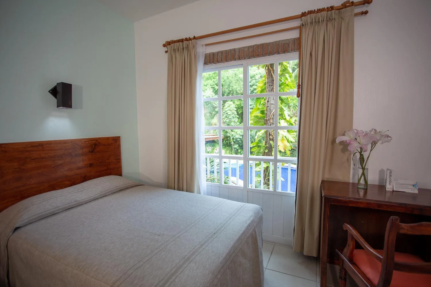 Standard room with one bed, desk, curtains, and leafy window view at Hotel Castillo Huatulco & Beach Club.