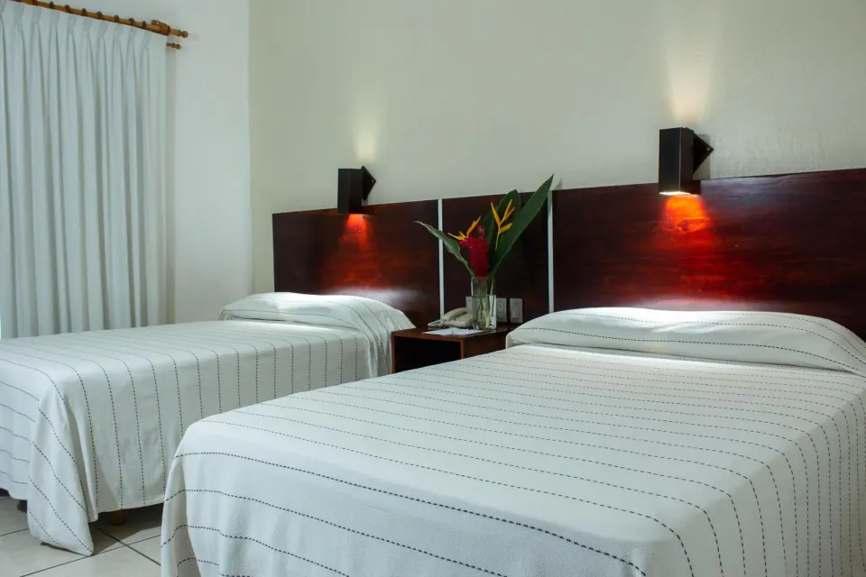 Standard room with two beds, dark wood headboards, and bedside flowers at Hotel Castillo Huatulco & Beach Club.