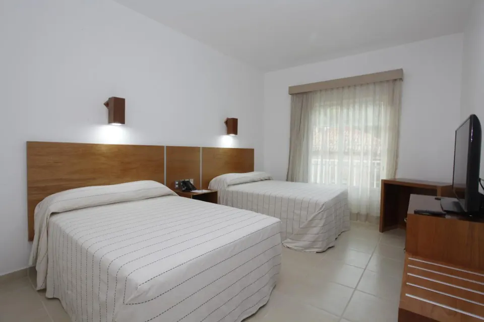 Standard room with two beds, TV, desk, and curtained window at Hotel Castillo Huatulco & Beach Club.