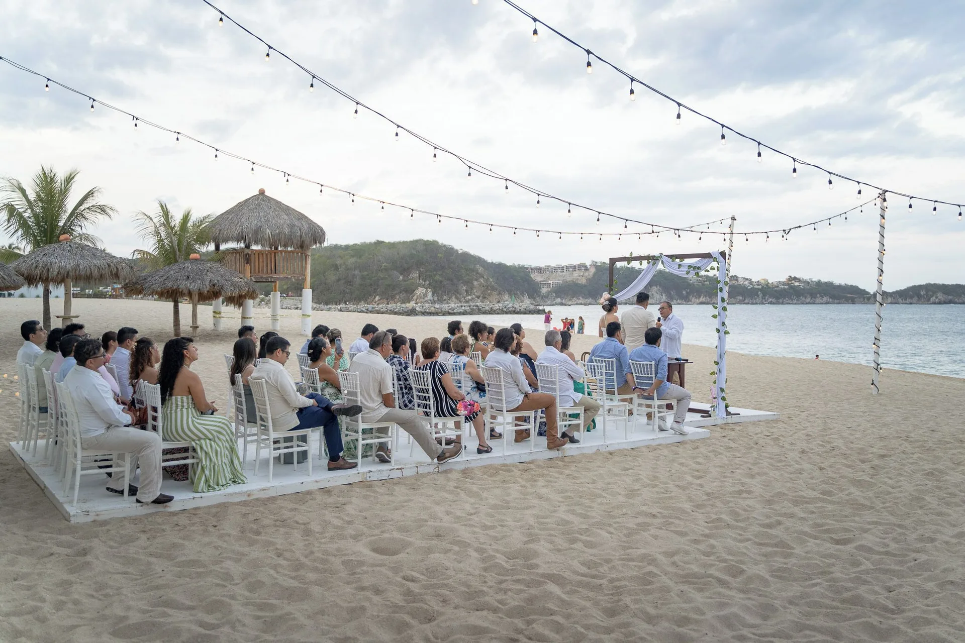 Side view of a beach wedding with white chairs and string lights at Hotel Castillo Huatulco & Beach Club.