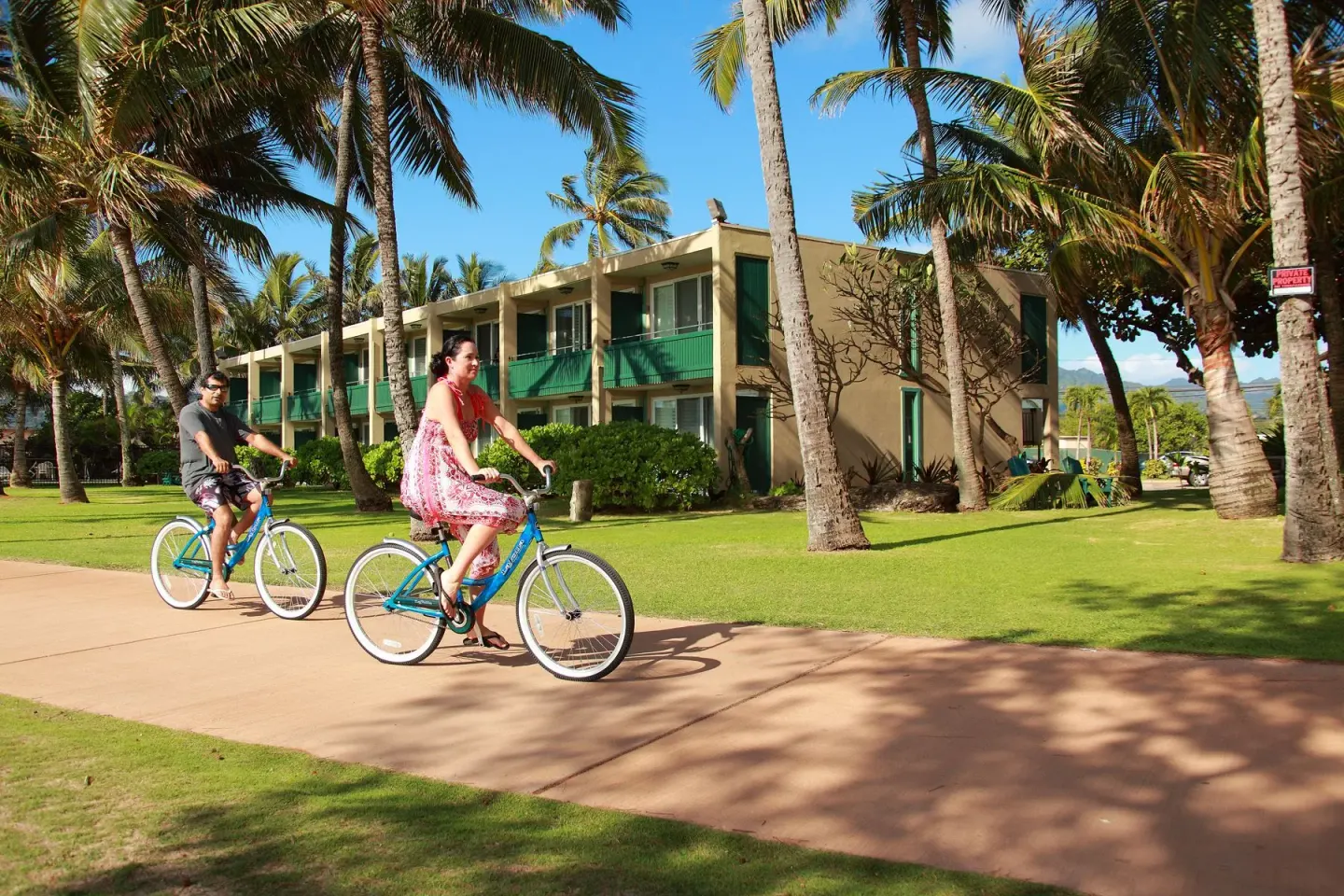 Guests riding bicycles past palms and resort rooms at Hotel Coral Reef.