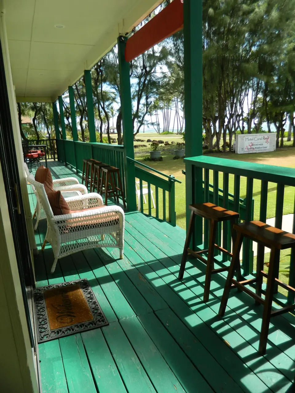 Green ocean-facing porch with wicker chairs and stools at Hotel Coral Reef.