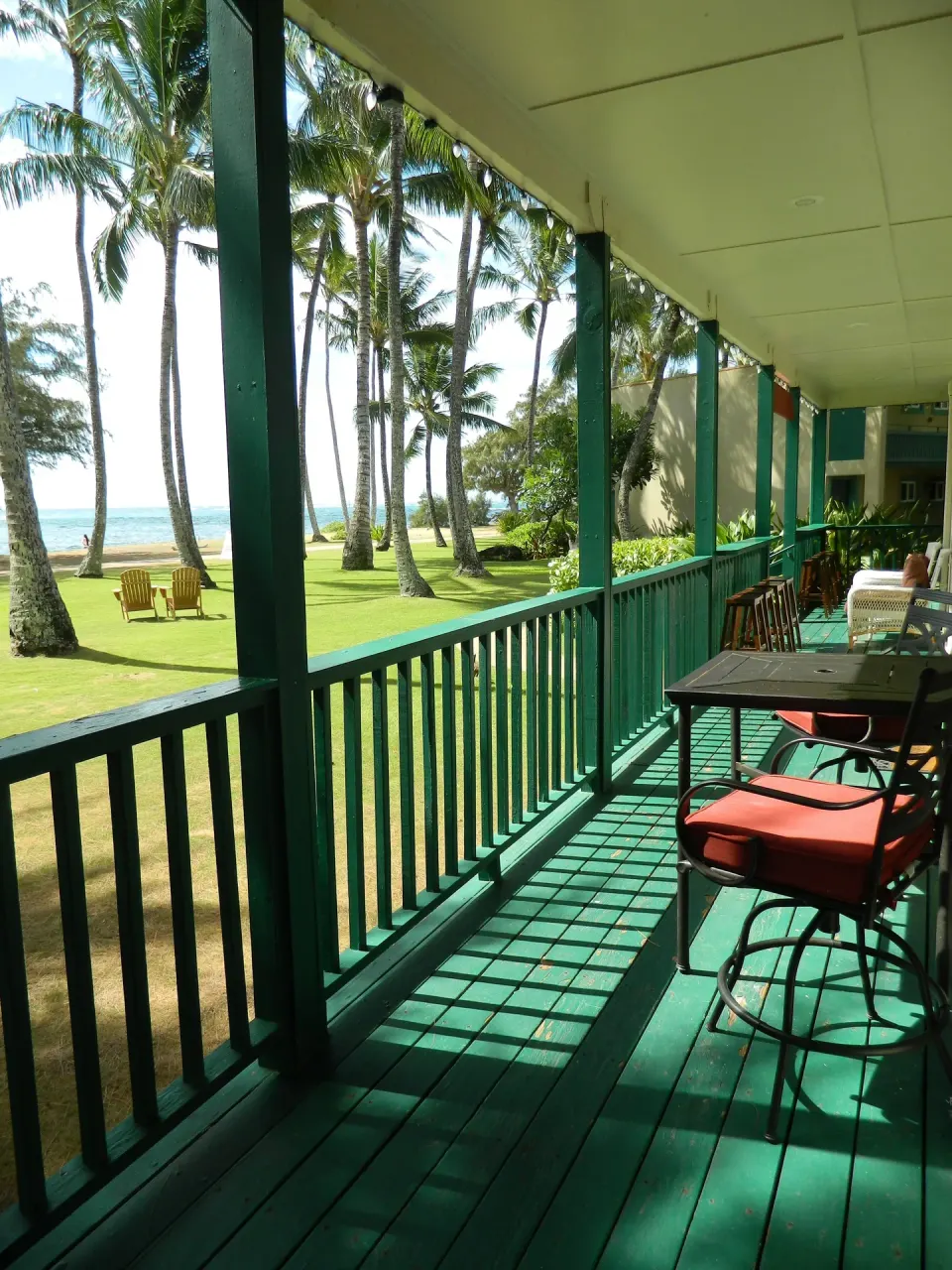 Covered balcony with chairs overlooking palms and ocean at Hotel Coral Reef.