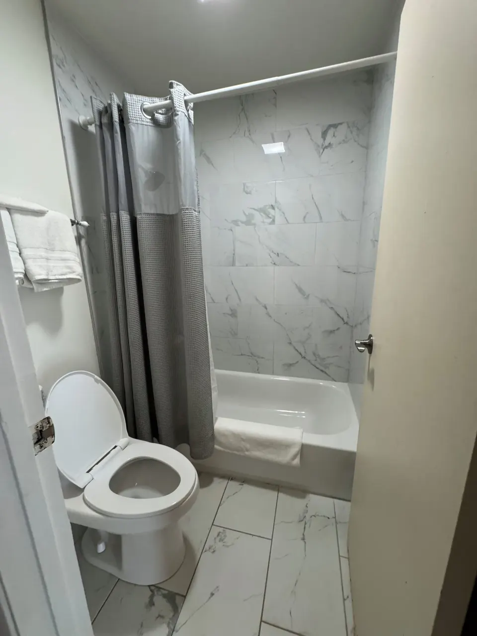 Economy Room City View bathroom with toilet, towels, tub, and gray shower curtain at Hotel Coral Reef.