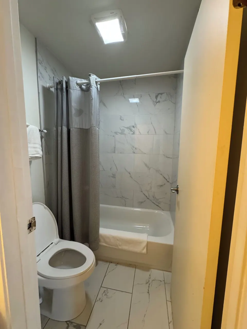 Economy Room City View bathroom with tub, toilet, gray curtain, and marble-look tile at Hotel Coral Reef.