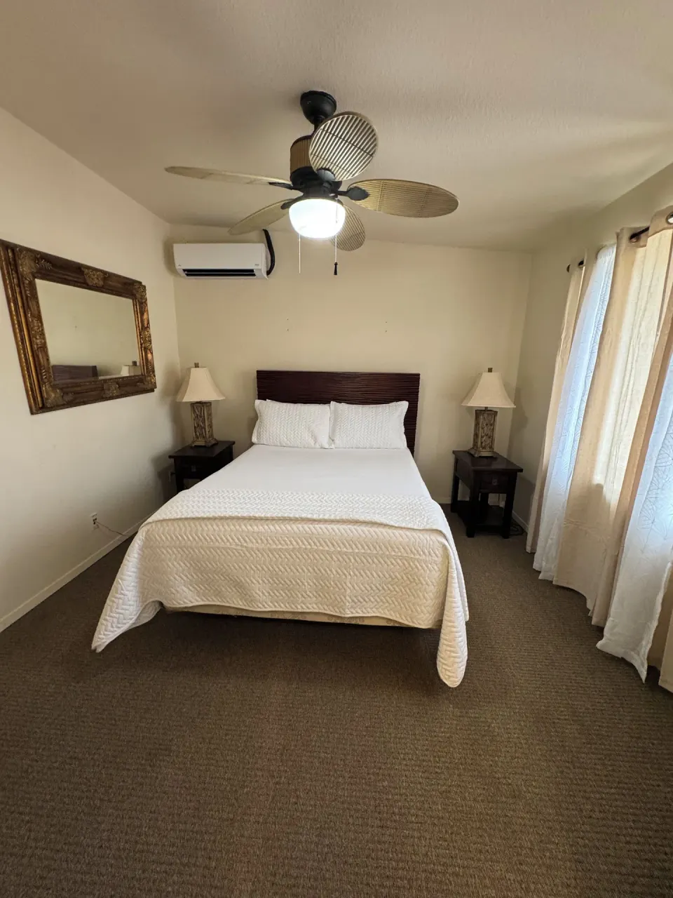 Economy Suite bedroom with white bed, nightstands, mirror, and ceiling fan at Hotel Coral Reef.