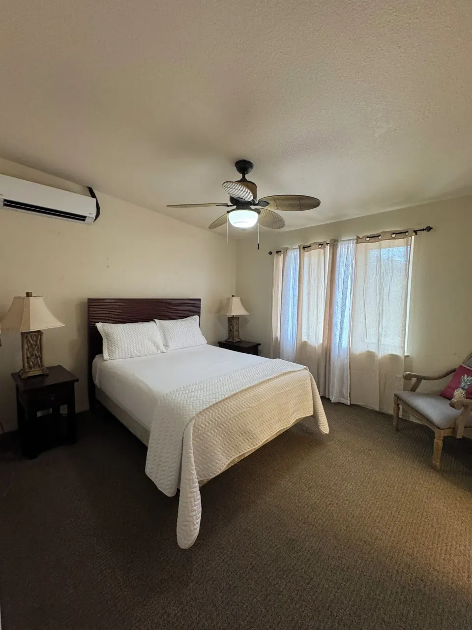 Economy Suite bedroom with queen bed, windows, armchair, and ceiling fan at Hotel Coral Reef.