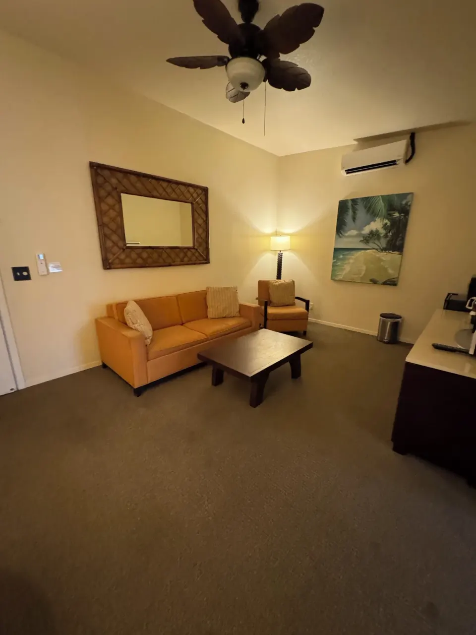 Economy Suite living area with orange sofa, chair, coffee table, and beach art at Hotel Coral Reef.