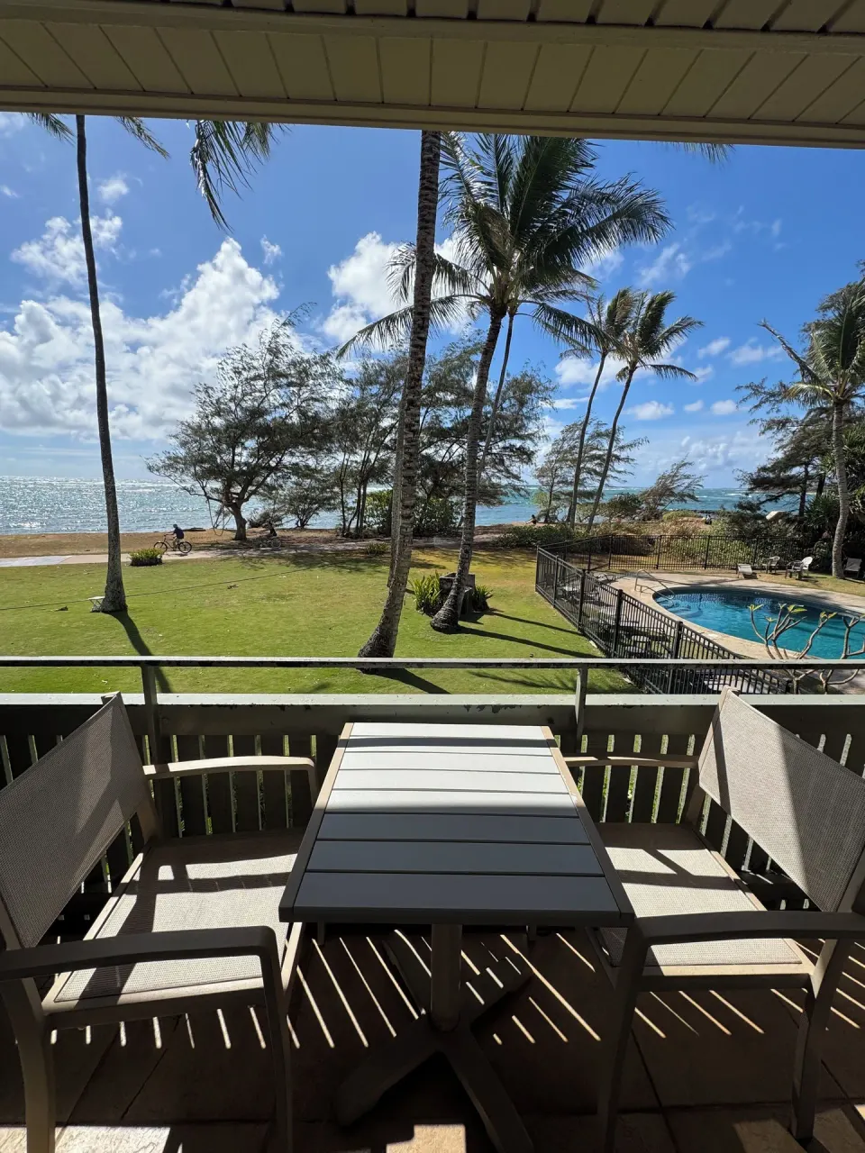 Ocean View balcony at Hotel Coral Reef with table, chairs, palms, ocean, lawn, and pool in view.