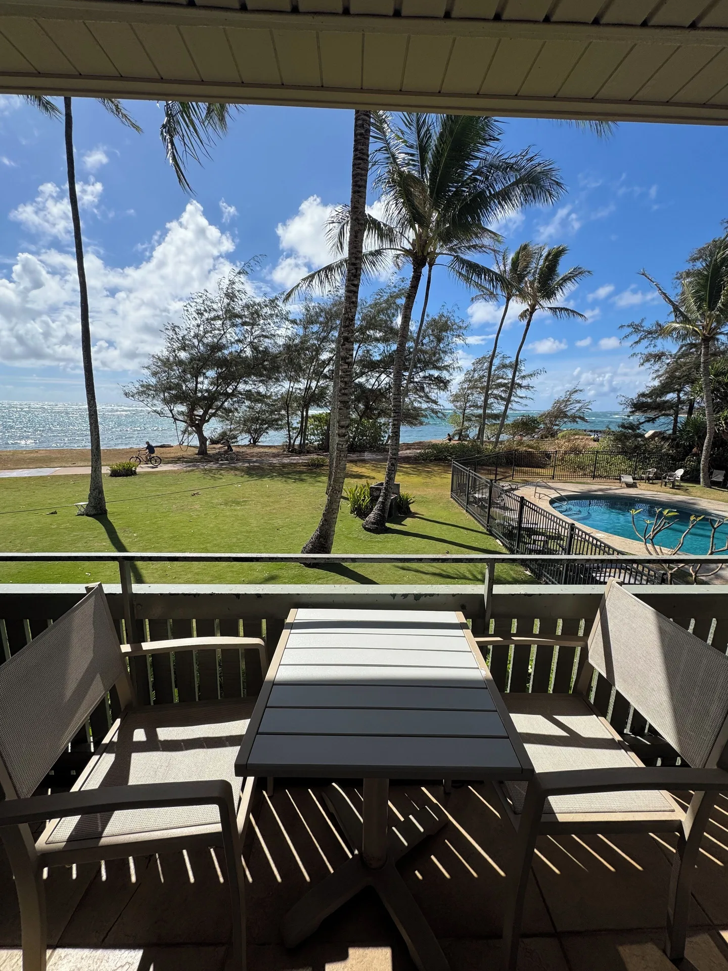 Ocean View balcony at Hotel Coral Reef with table, chairs, palms, ocean, lawn, and pool in view.