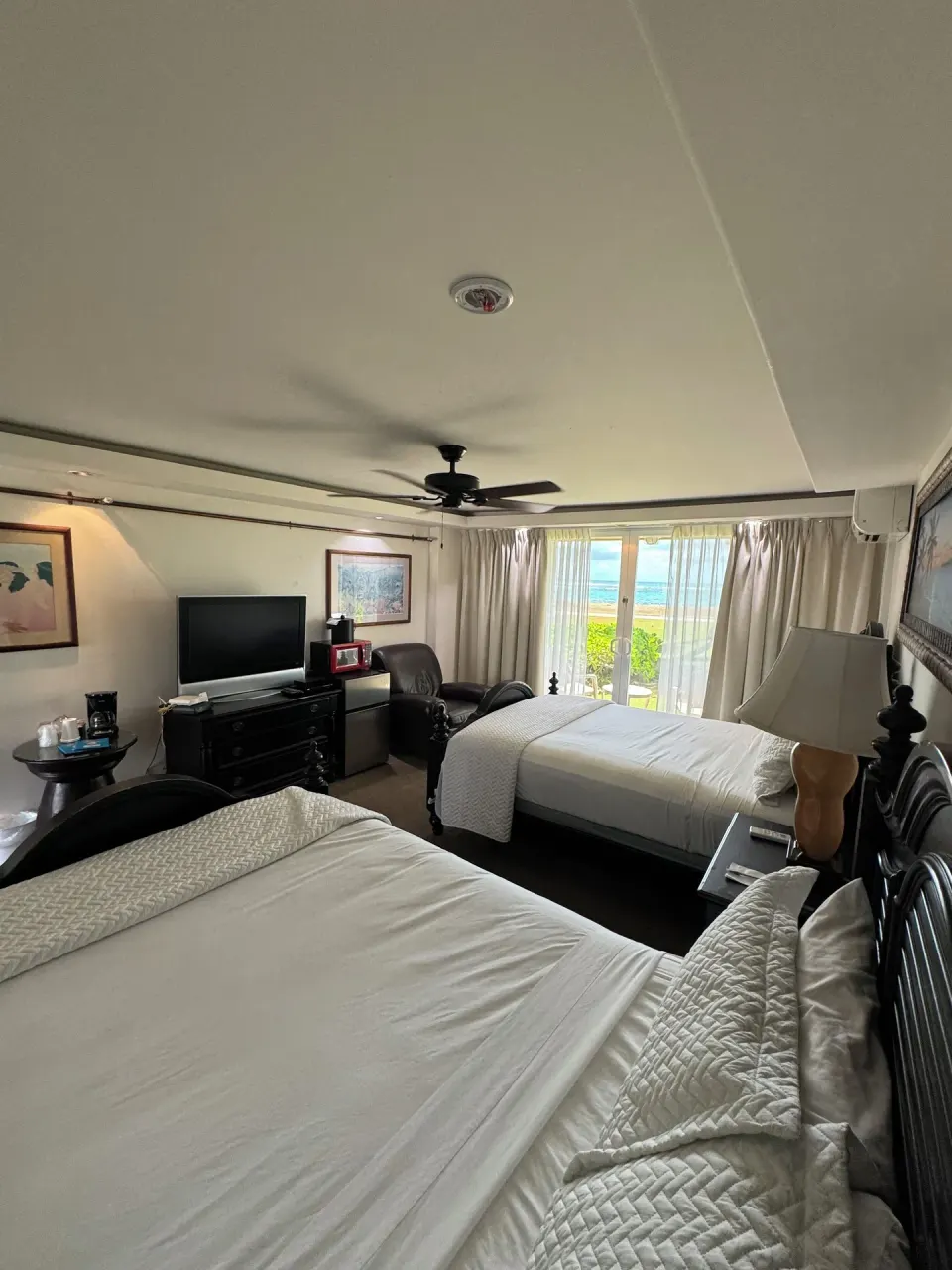 Ocean View room at Hotel Coral Reef with two beds, seating, TV, and ocean visible through glass doors.