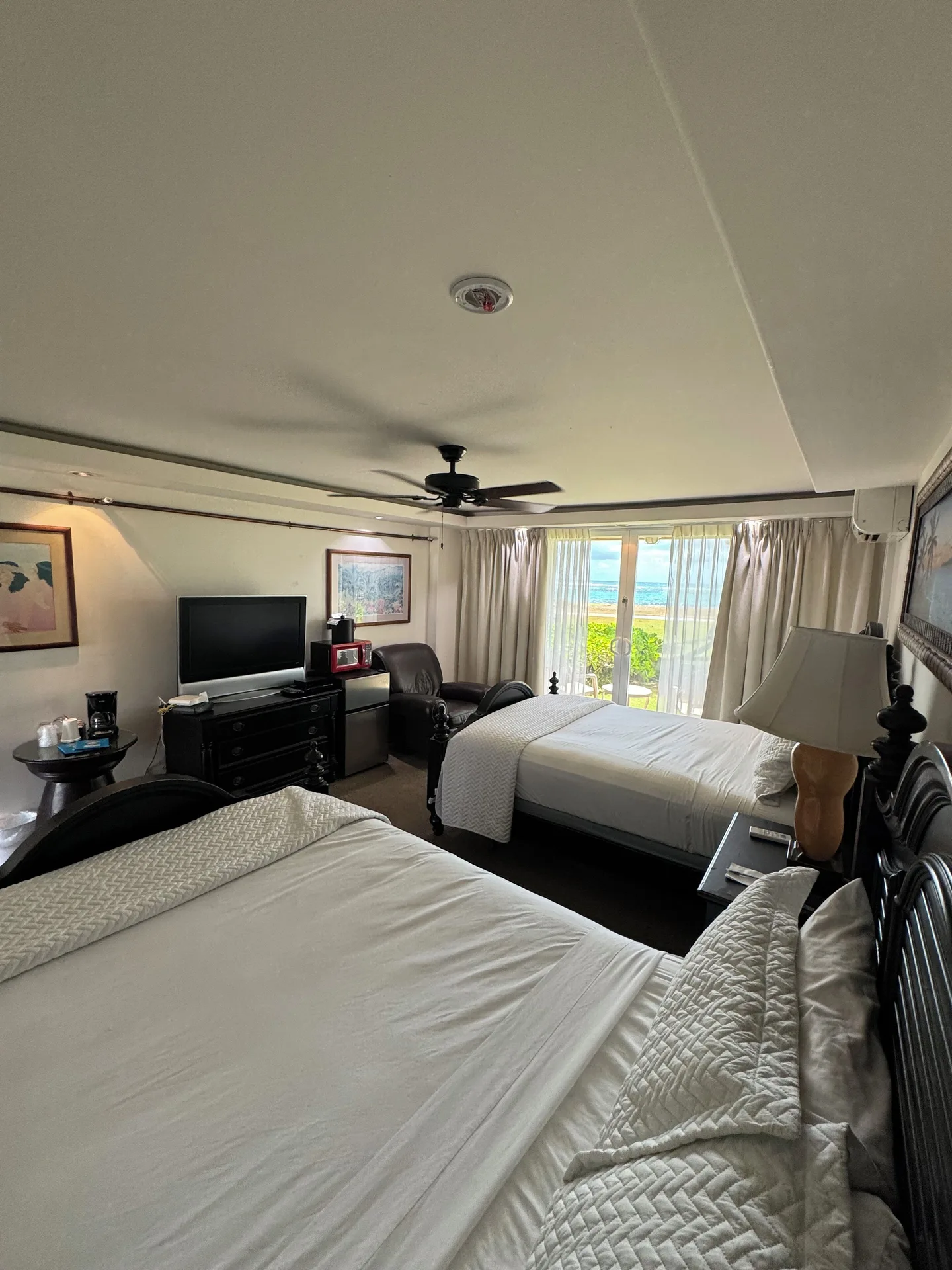 Ocean View room at Hotel Coral Reef with two beds, seating, TV, and ocean visible through glass doors.