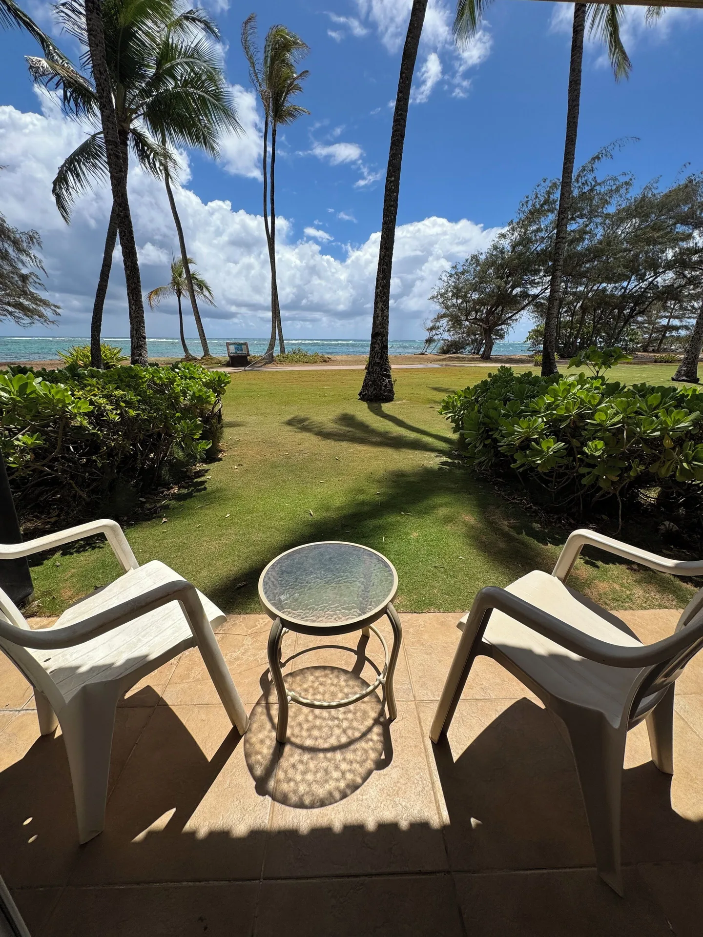 Oceanfront patio at Hotel Coral Reef with two chairs, a small table, lawn, palms, and ocean beyond.