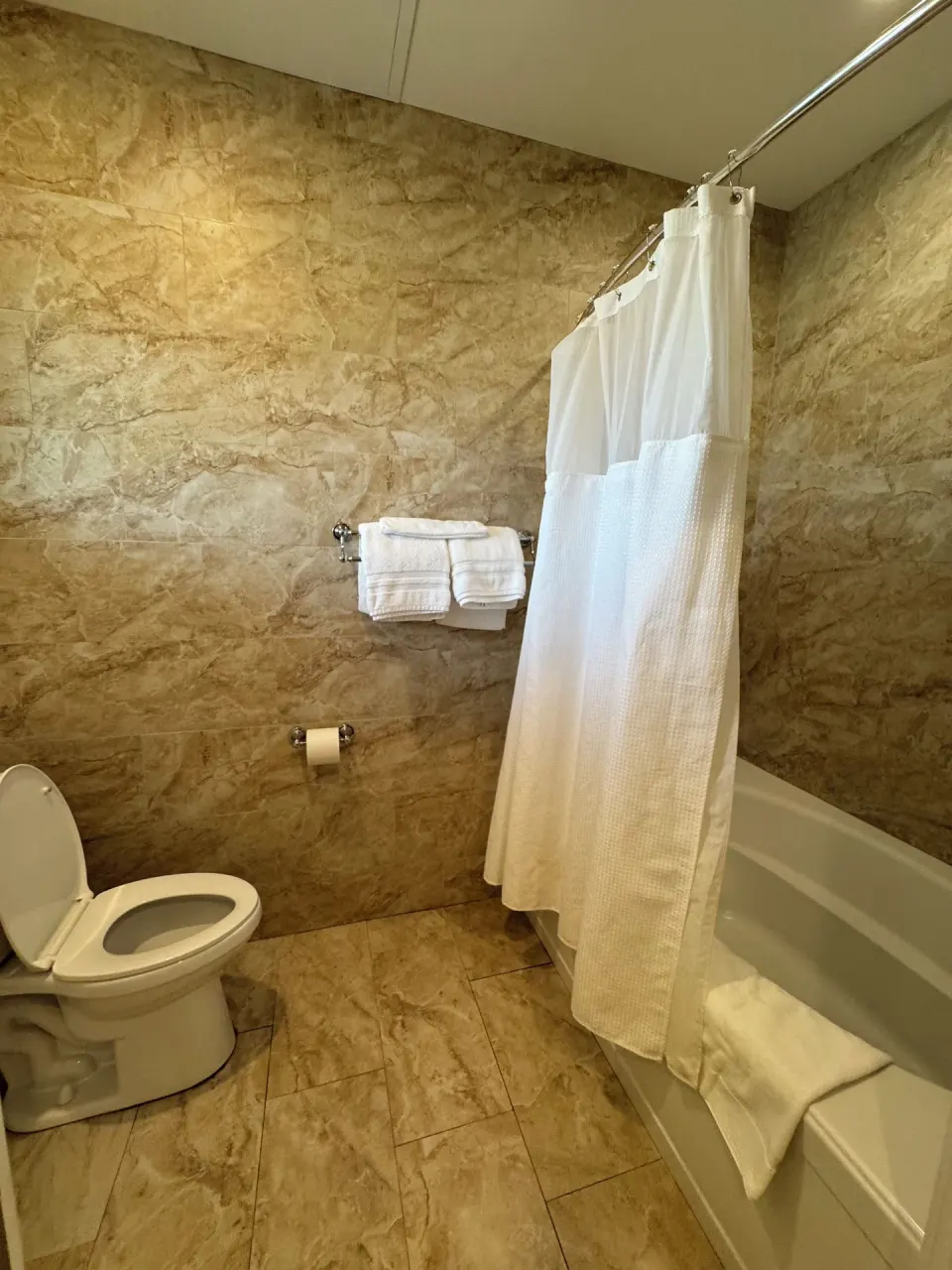 Premium Suite tiled bathroom with tub, towels, and white shower curtain at Hotel Coral Reef.
