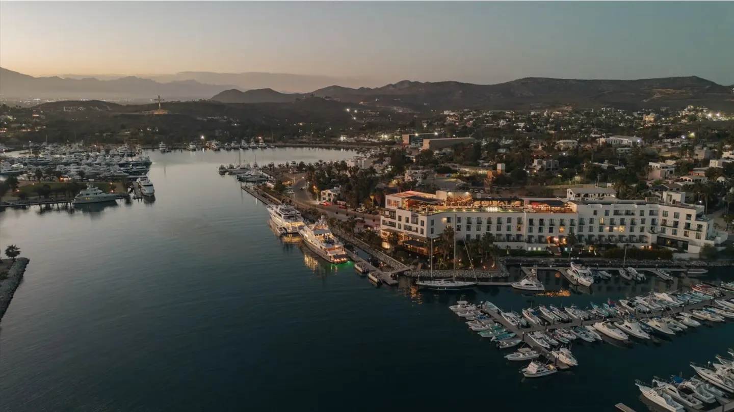 Aerial dusk view of Hotel El Ganzo beside the marina, town lights, and surrounding hills.