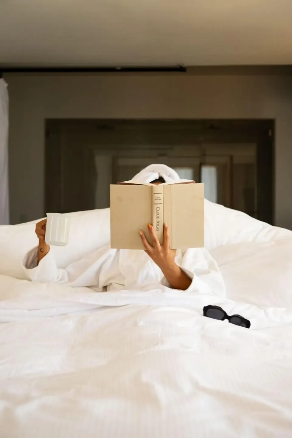 Guest relaxing in a white bed with a book and cup at Hotel El Ganzo.