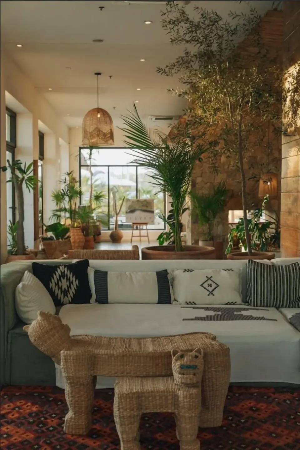 Lobby lounge with a white sofa, woven animal figures, and indoor plants at Hotel El Ganzo.
