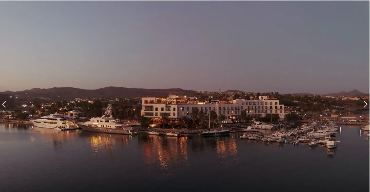 Hotel El Ganzo by the marina at dusk with boats and water reflections.