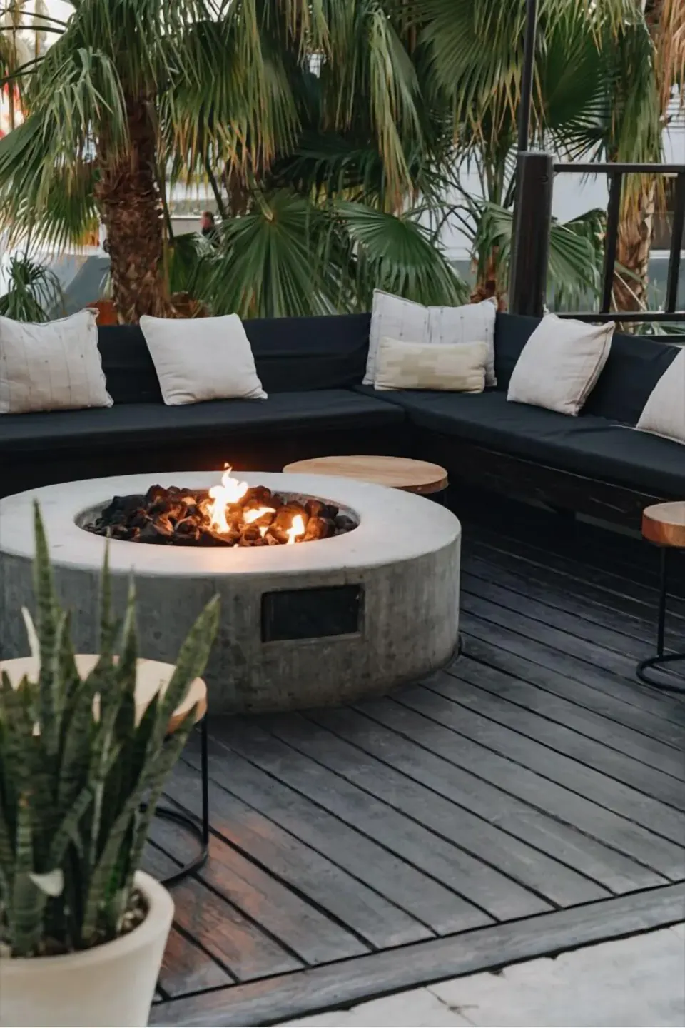 Outdoor lounge at Hotel El Ganzo with a round fire pit, cushioned seating, palms, and side tables.