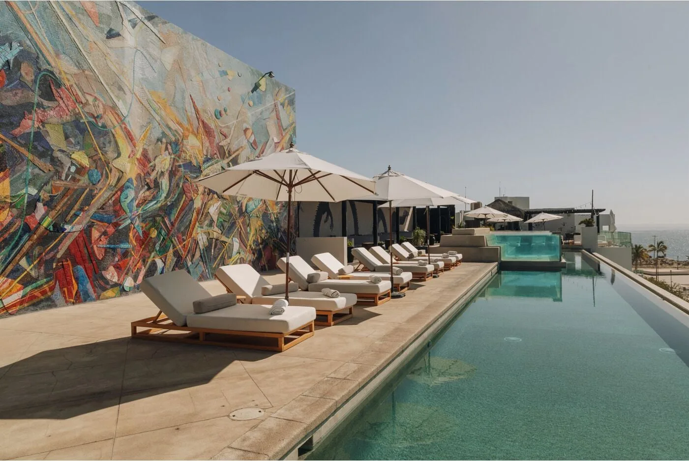 Rooftop pool deck with loungers, umbrellas, and mural at Hotel El Ganzo.