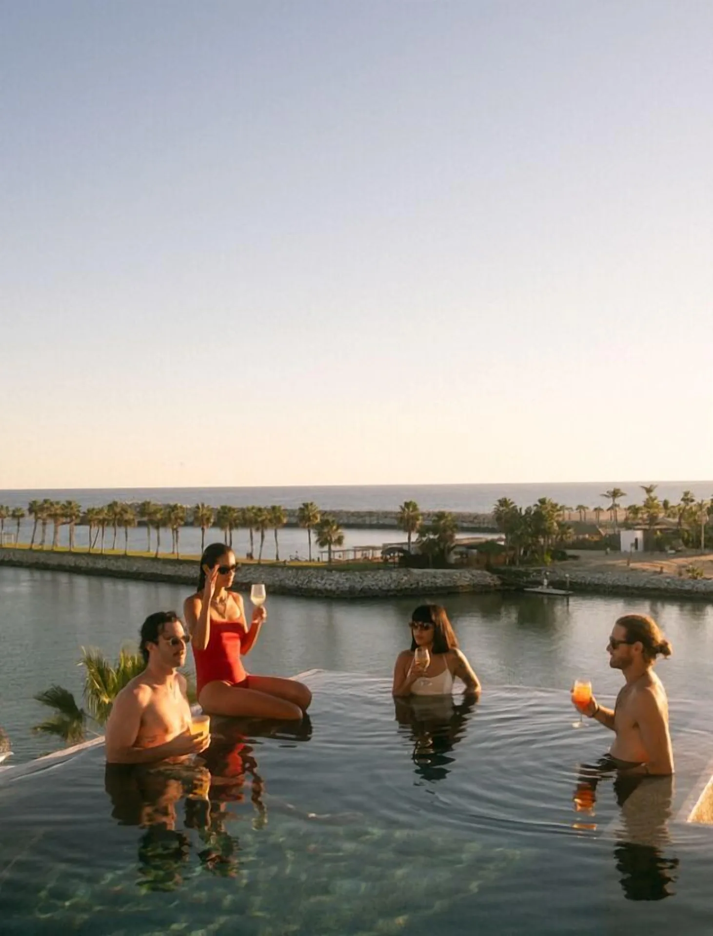 Guests holding drinks in an infinity pool at sunset at Hotel El Ganzo.