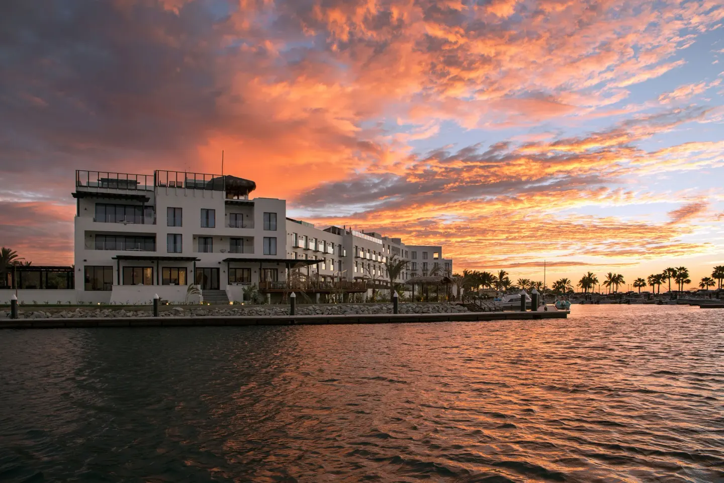 Hotel El Ganzo waterfront exterior at sunset with orange clouds over the marina.