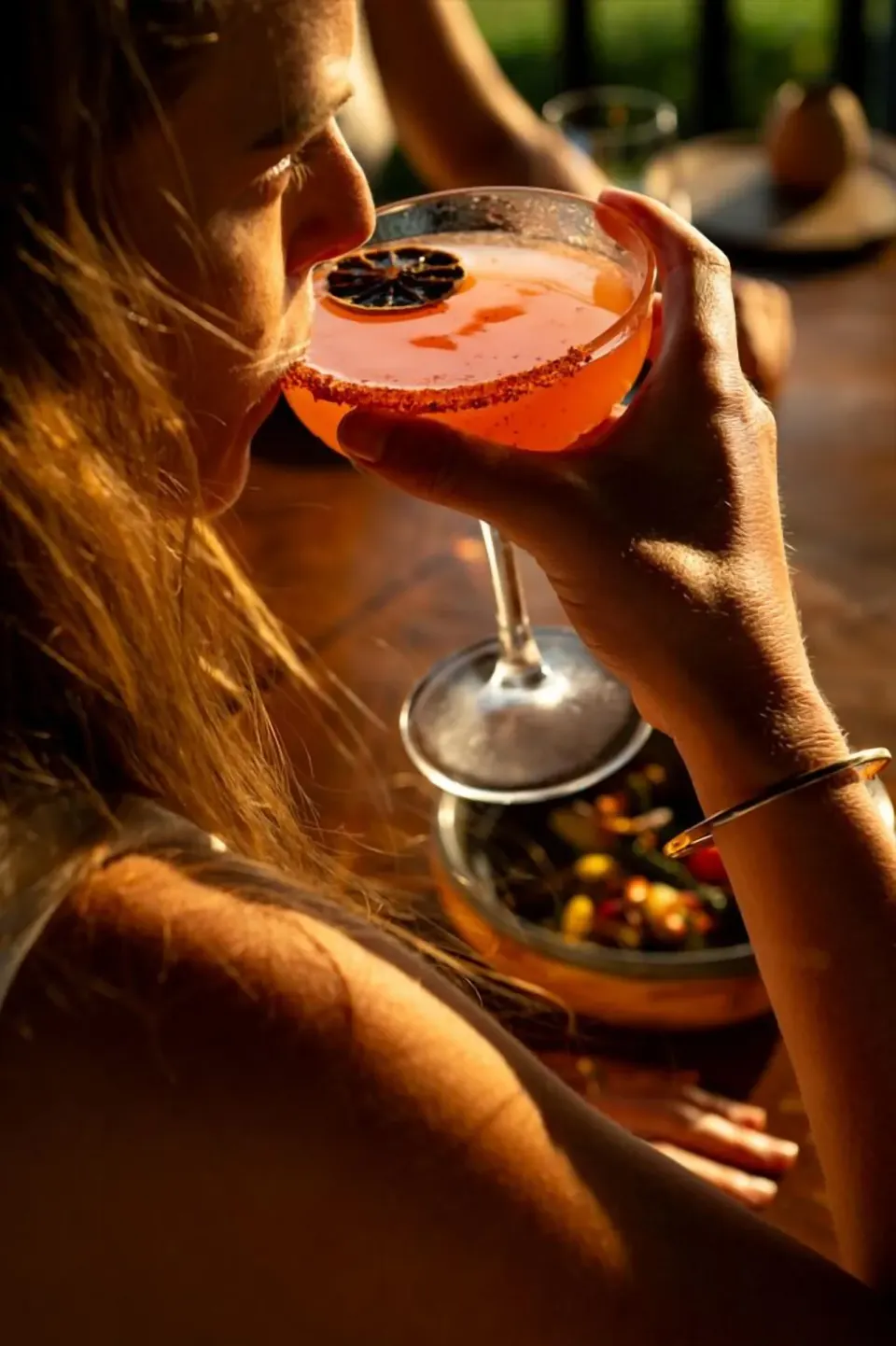 A guest sips a citrus-garnished cocktail in warm light at Hotel El Ganzo.