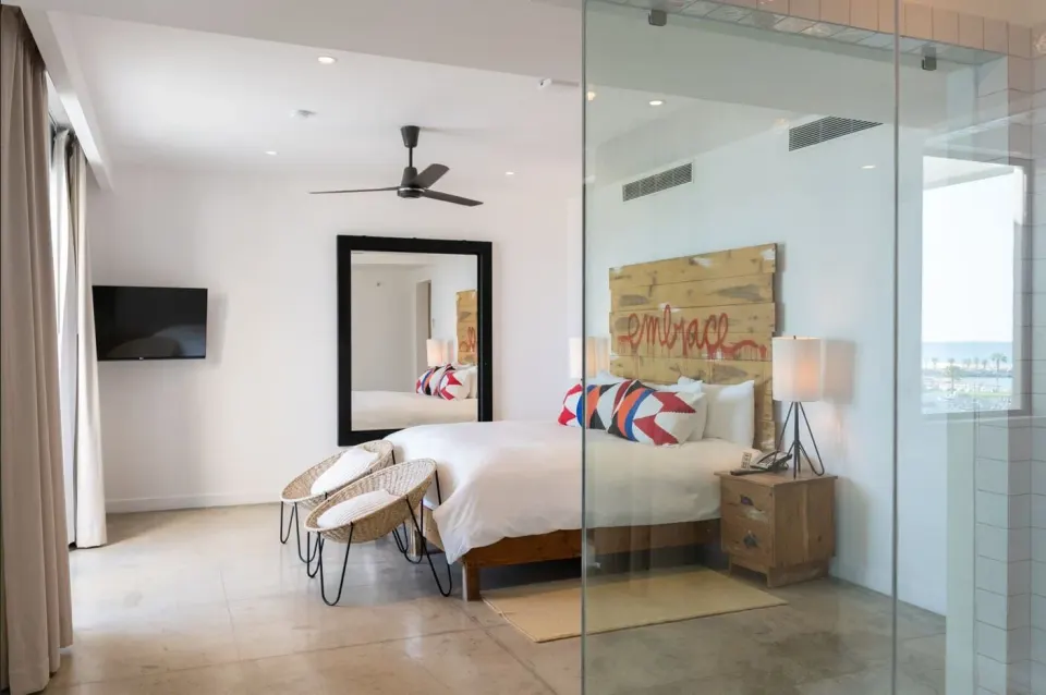 Penthouse Suite One Bedroom king bed at Hotel El Ganzo beside a glass-walled bathroom and sitting chairs.