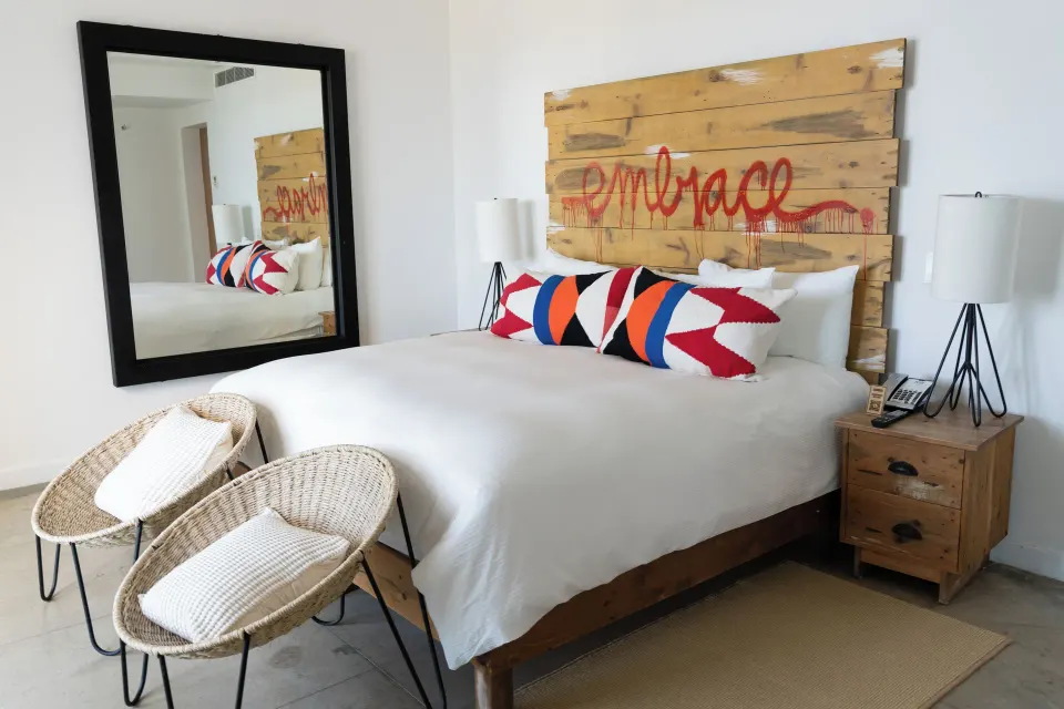 Penthouse Suite One Bedroom king bed at Hotel El Ganzo with wood headboard, colorful pillows, and woven chairs.