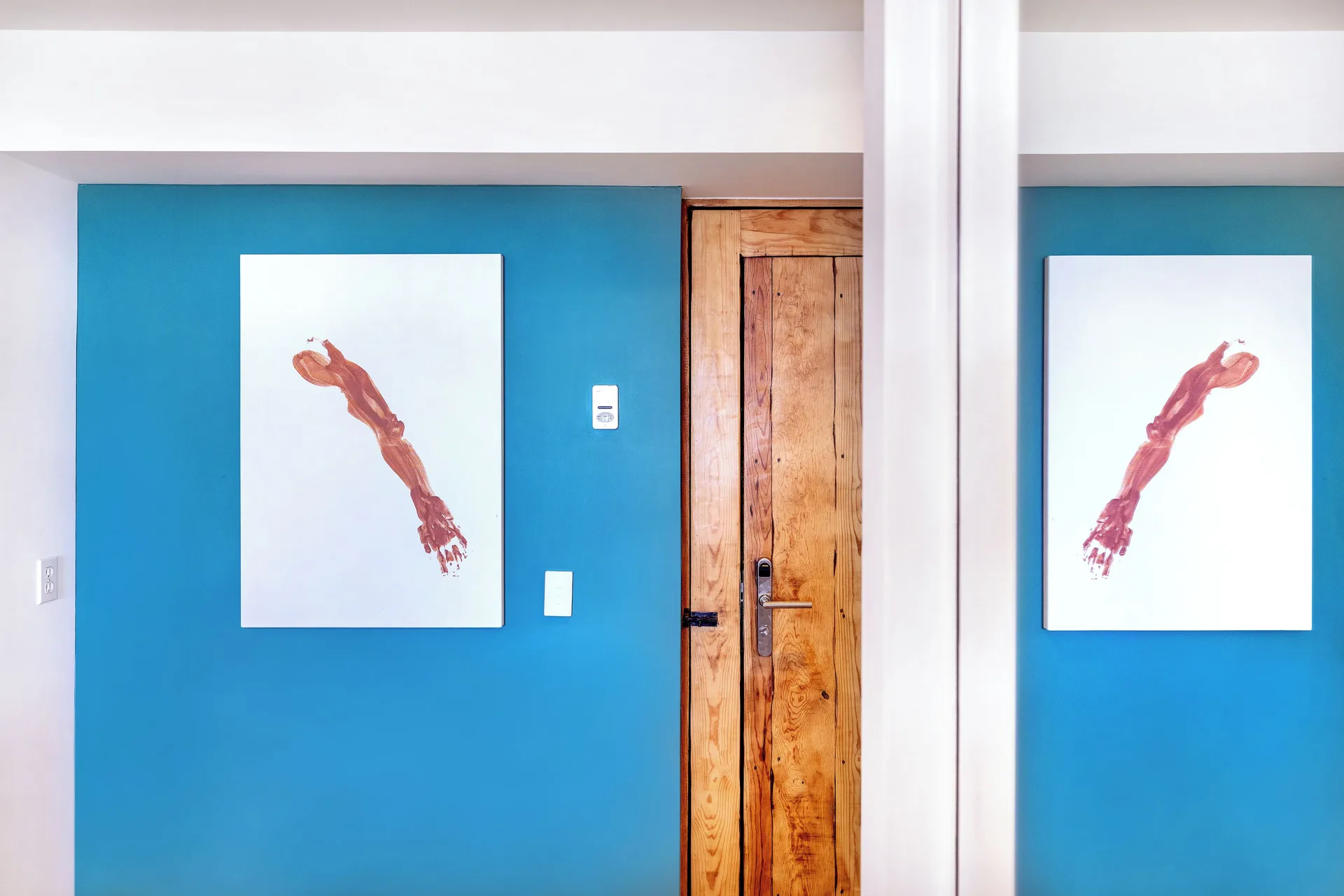 Standard Suite entry wall with blue paint, wood door, and artwork at Hotel El Ganzo.