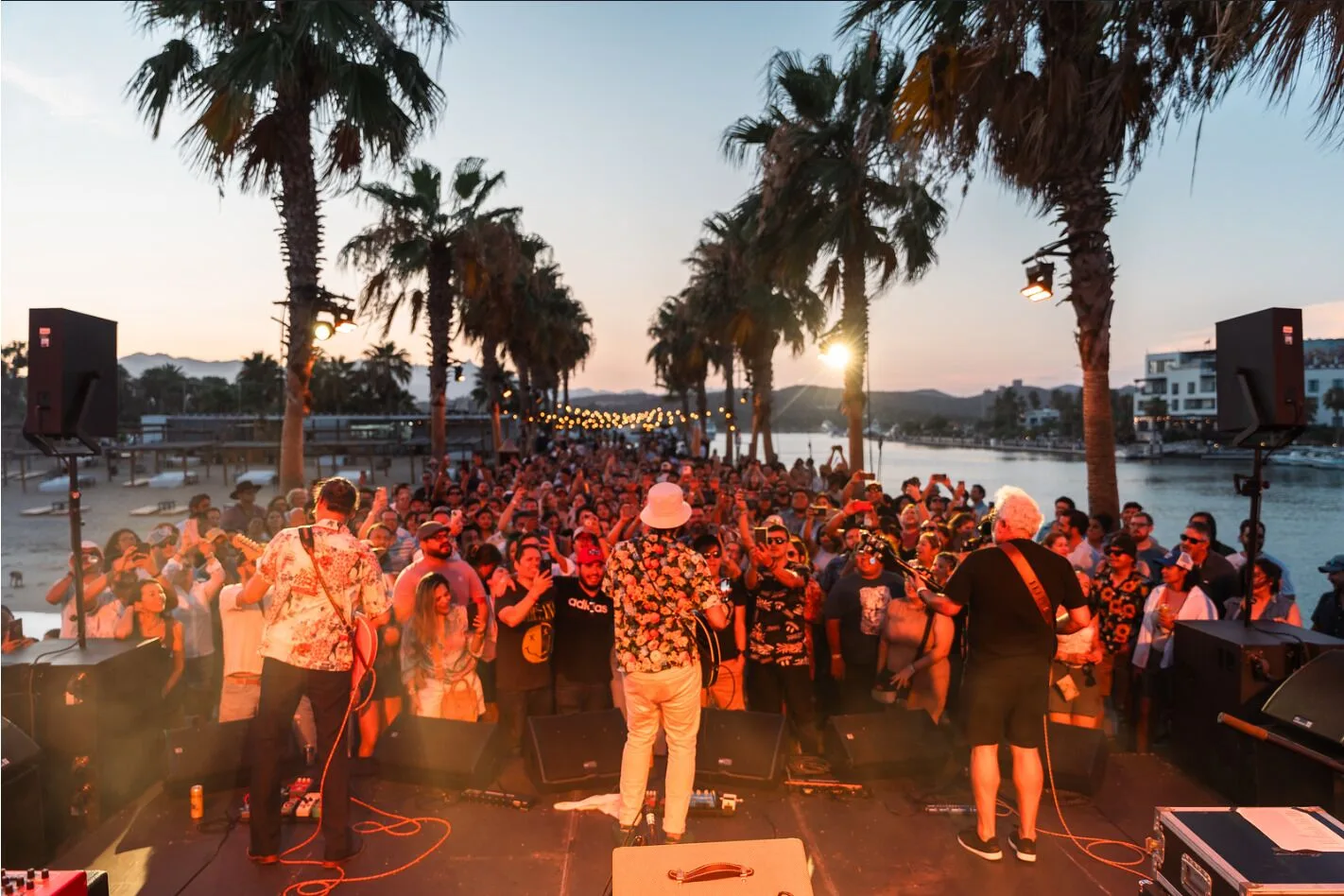 Live outdoor concert at Hotel El Ganzo with a band onstage, crowd, palms, and marina at sunset.