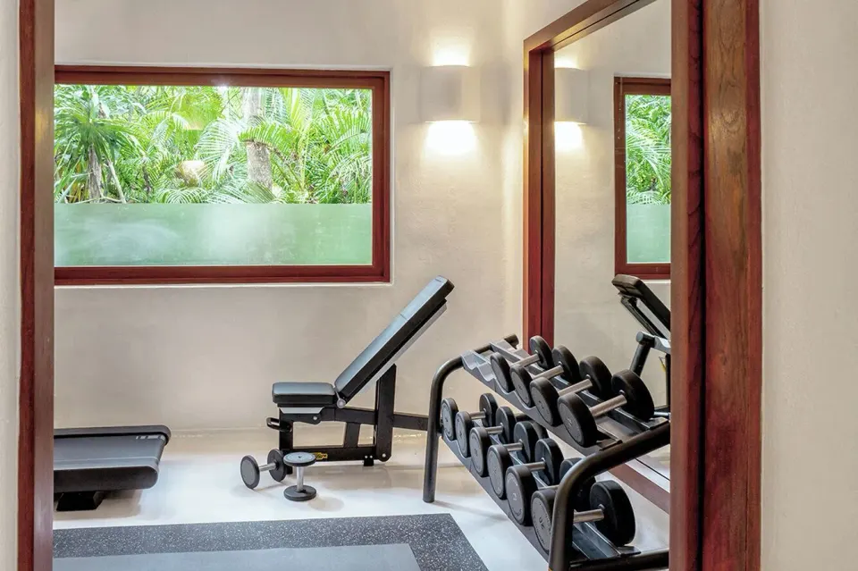 Gym corner with dumbbell rack, adjustable bench and window at Hotel Esencia.