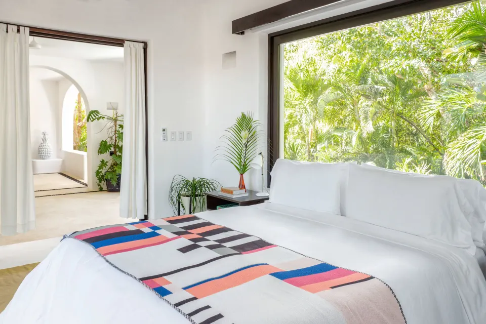 Bright bed next to a large window framed by lush tropical foliage at Hotel Esencia.