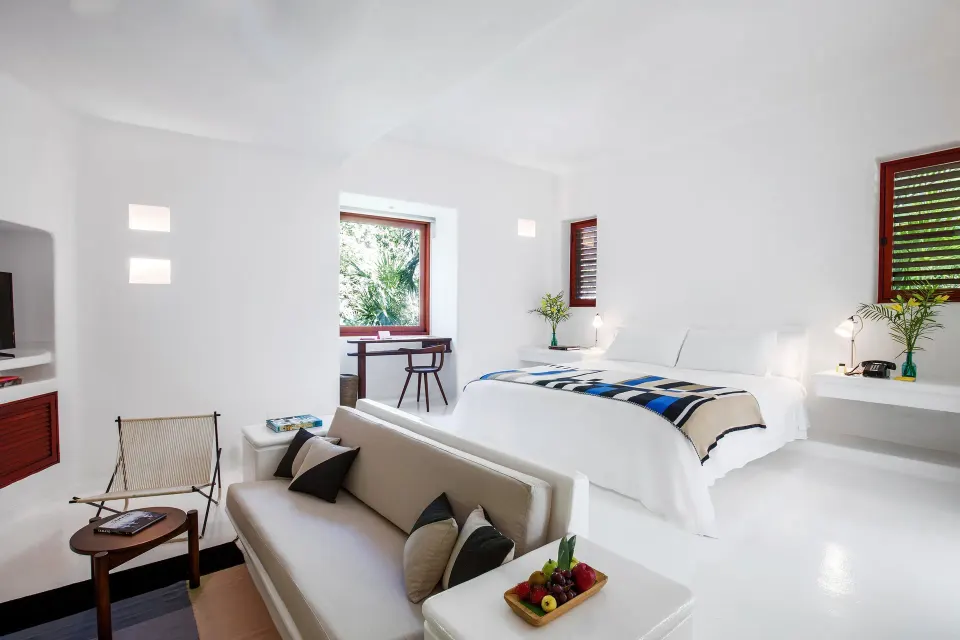 White suite with freestanding tub and doors opening to a leafy deck at Hotel Esencia.