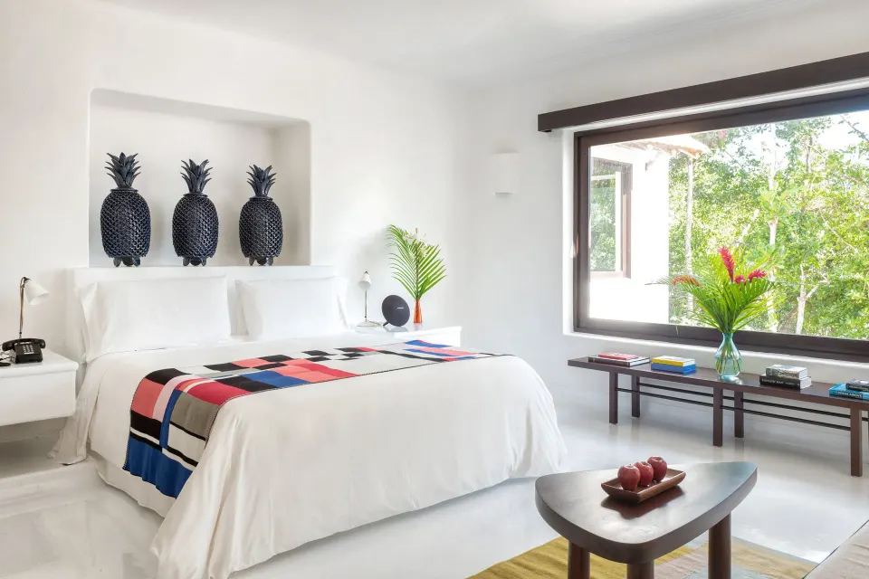 Bright guest room with king bed, decorative wall pineapples and garden views at Hotel Esencia