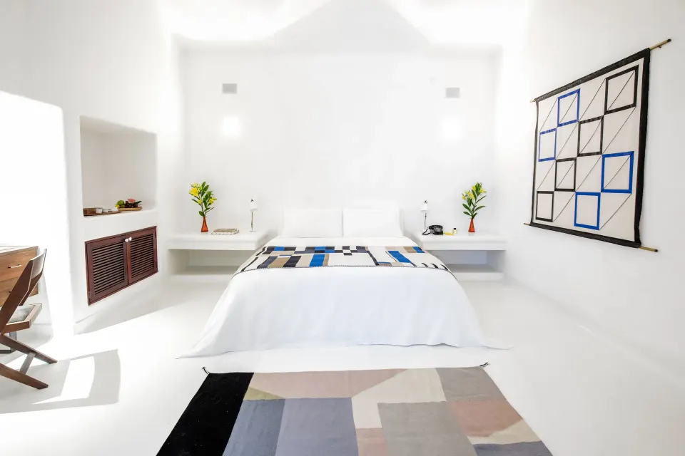 Minimalist white bedroom with geometric wall hanging at Hotel Esencia.