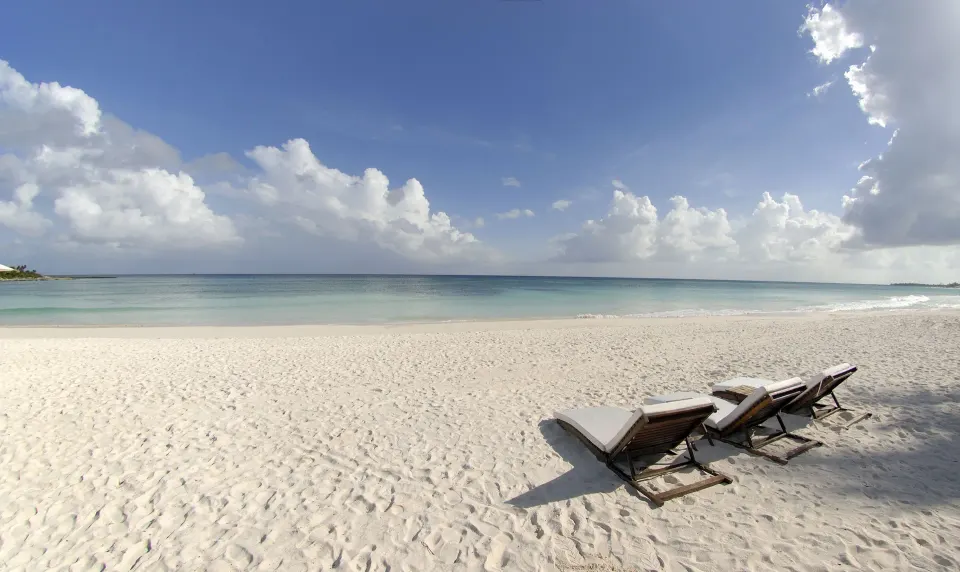 Two lounge chairs on a wide white sand beach under a blue sky at Hotel Esencia