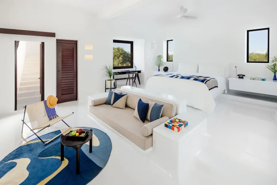 Spacious white suite at Hotel Esencia with bed, sofa and seating area.
