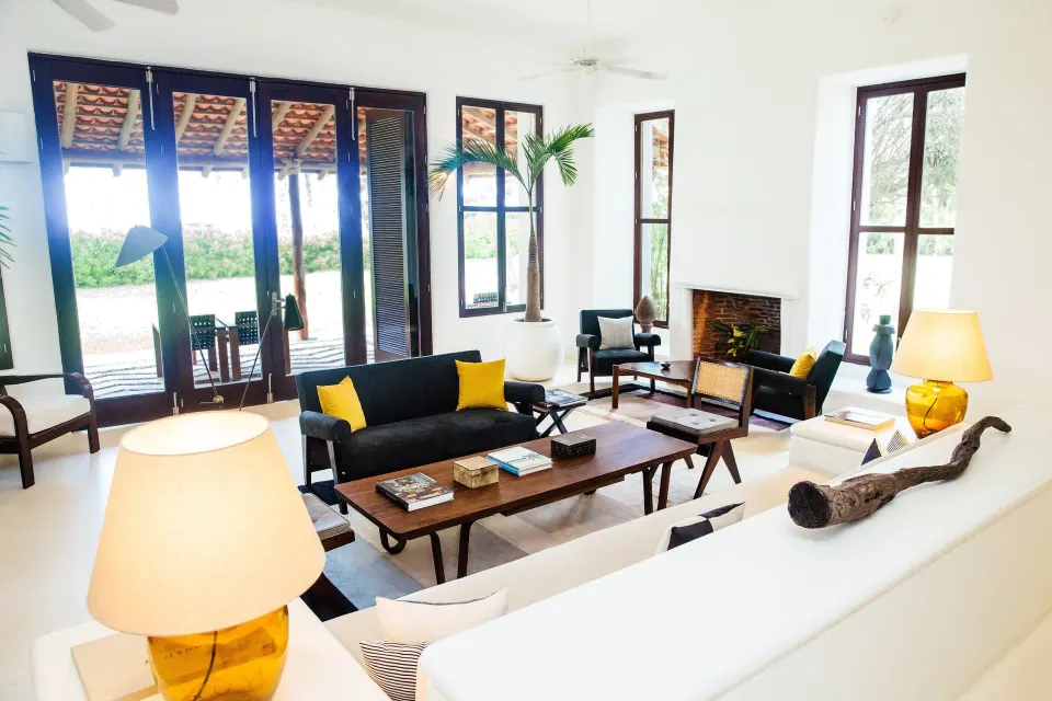 Bright white living room with dark wood furniture and yellow accents at Hotel Esencia.