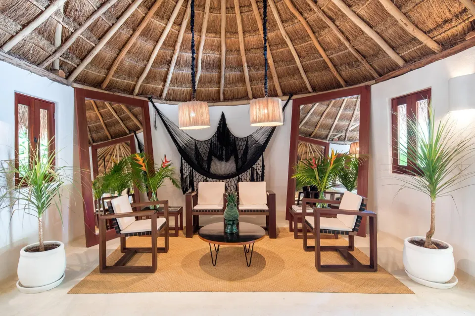 Thatched circular lounge with wooden chairs and tropical plants at Hotel Esencia.
