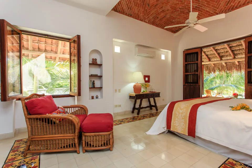Warm traditional room with wicker seating and an arched doorway opening to a thatched outdoor area at Hotel Esencia.