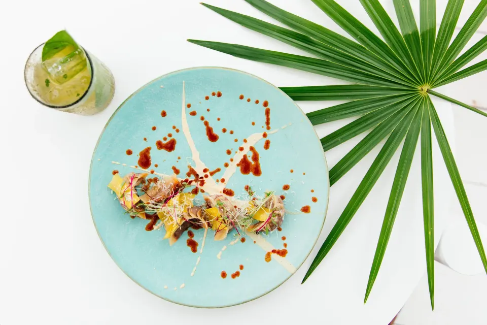 Artful plated dish on a turquoise plate with a palm leaf at Hotel Esencia.